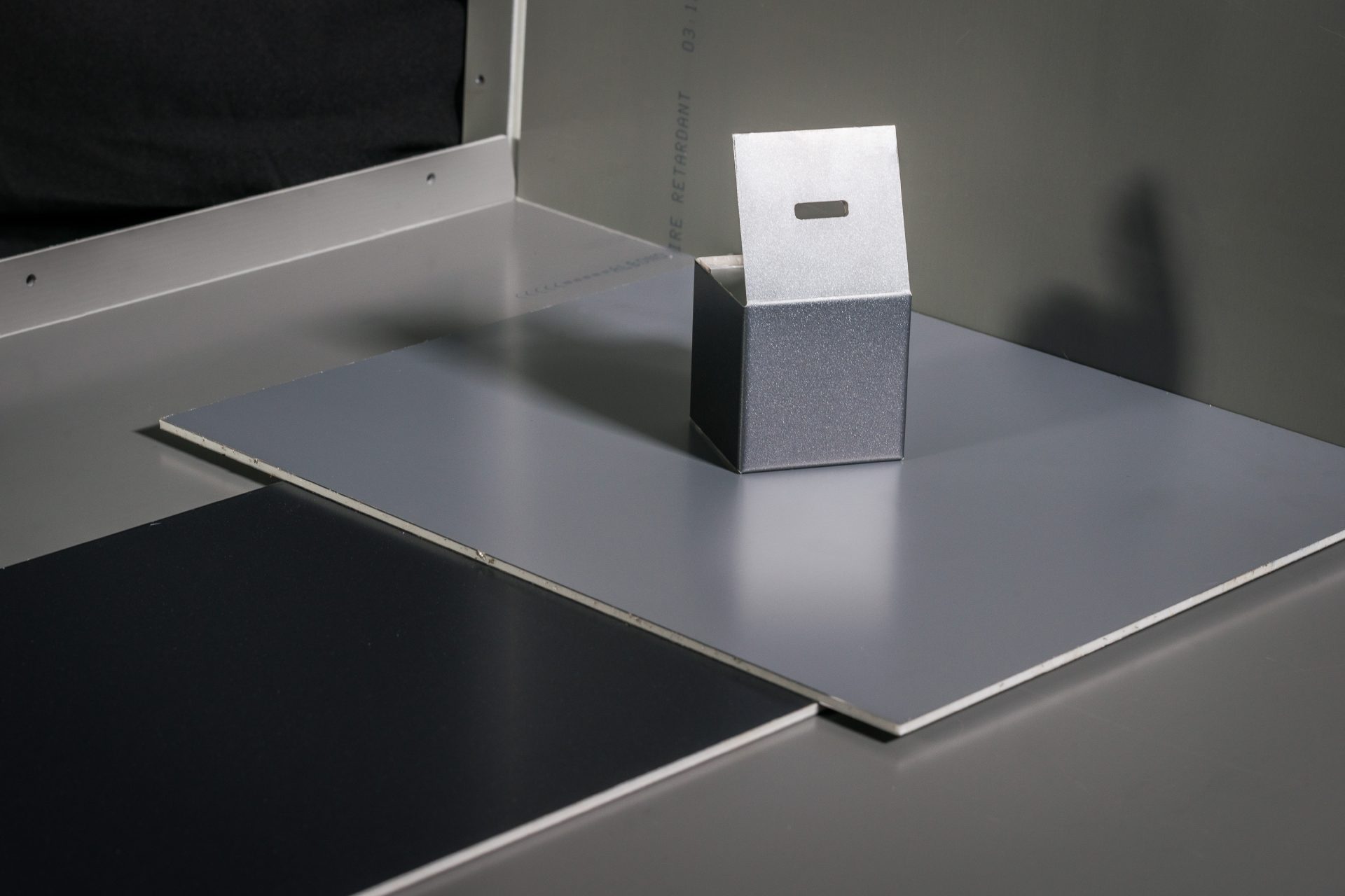 Silver casing made of composite panels standing on a grey plate next to a black rectangular insert.