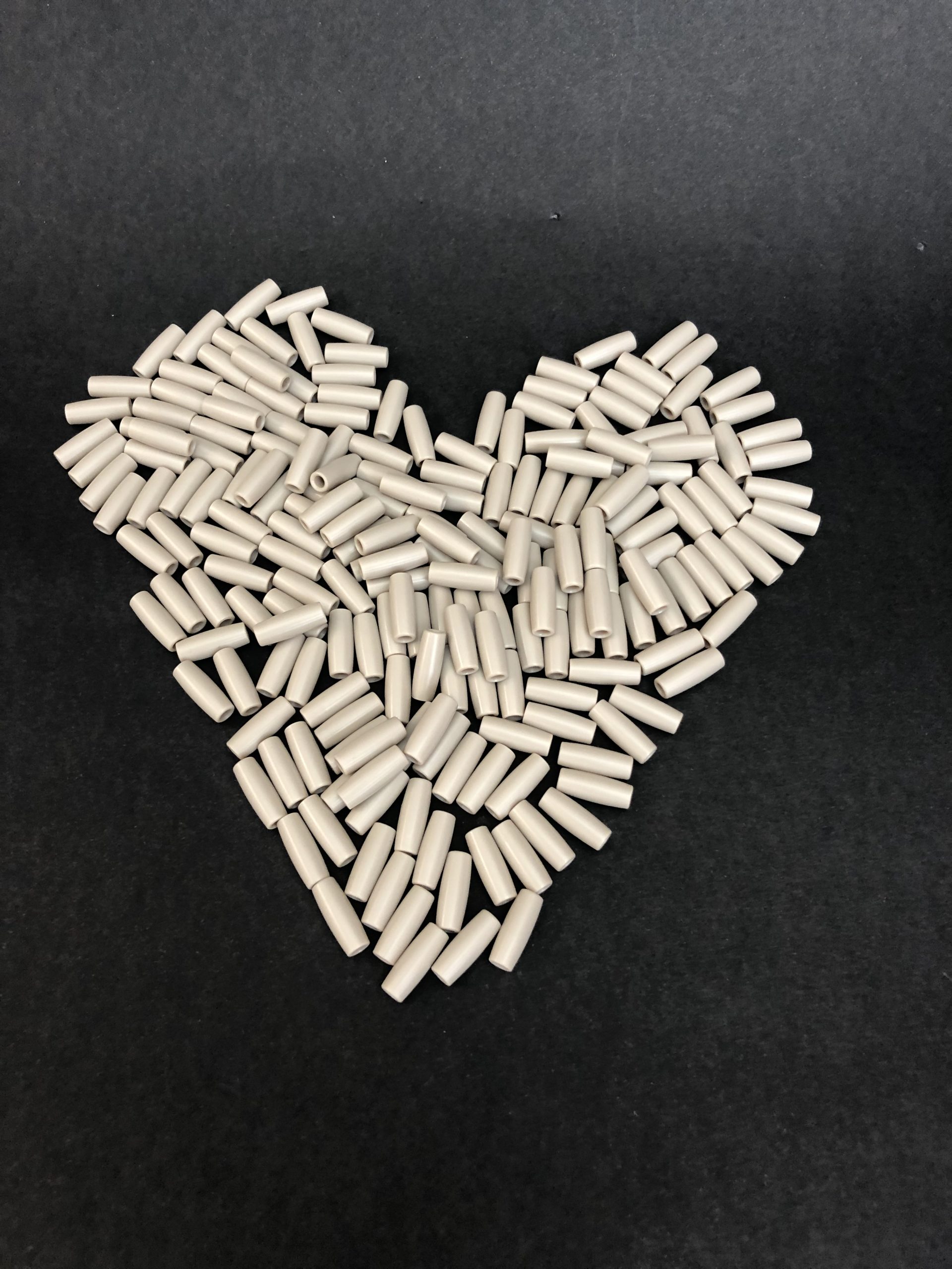 Numerous small beige plastic rollers arranged in the shape of a heart against a uniform black background.