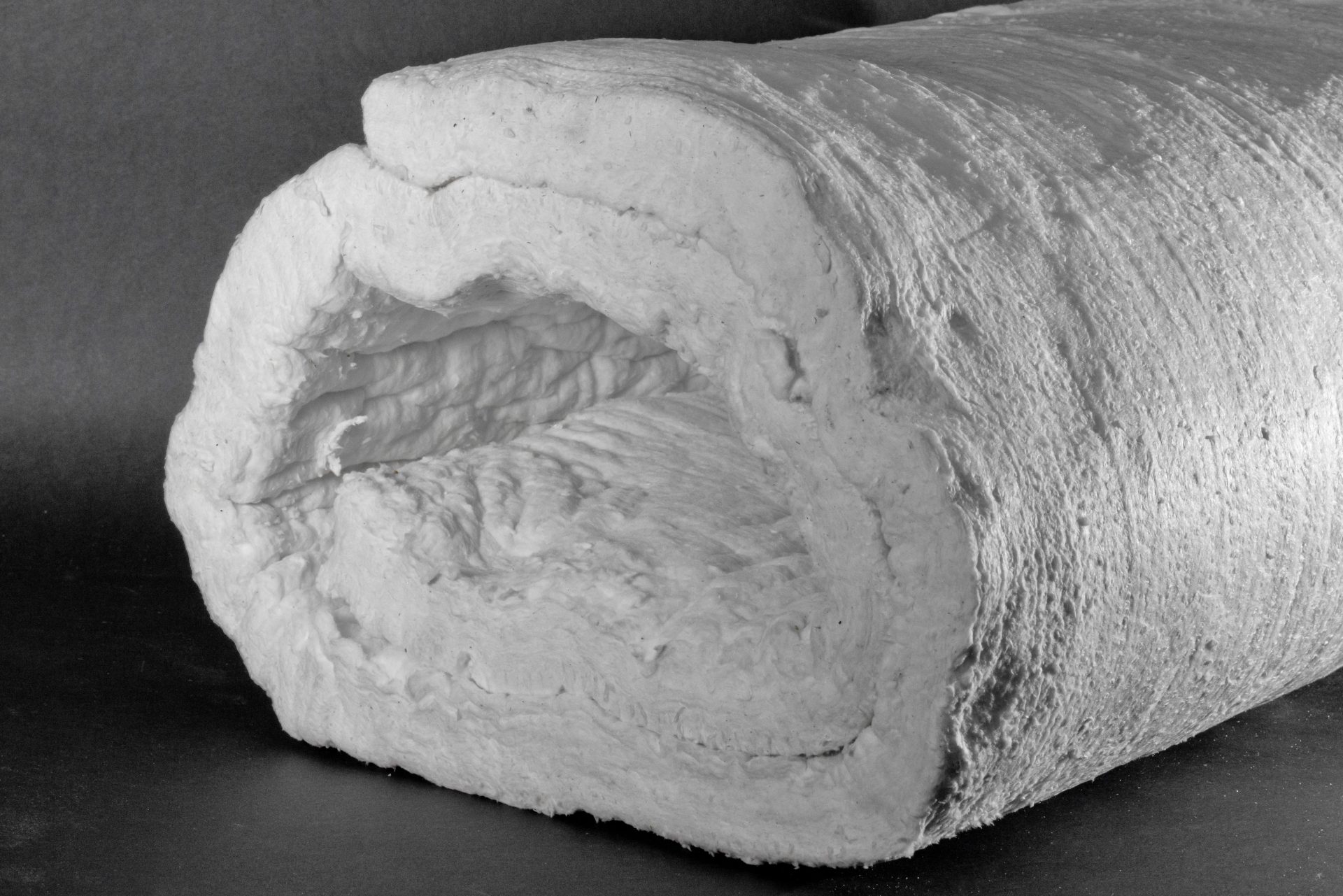 A large roll of white, fluffy fibrous insulation material against a dark plain background.