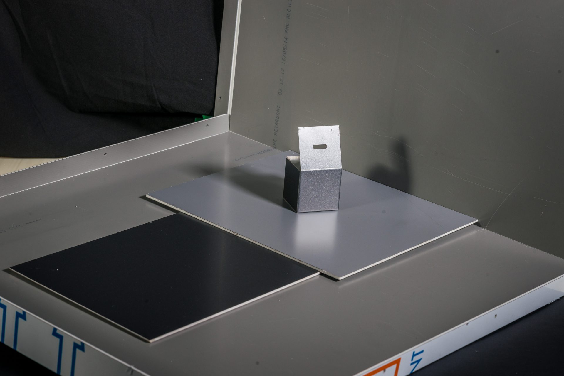 Photograph of a metal platform, two square plates in black and grey, and a small metal part.