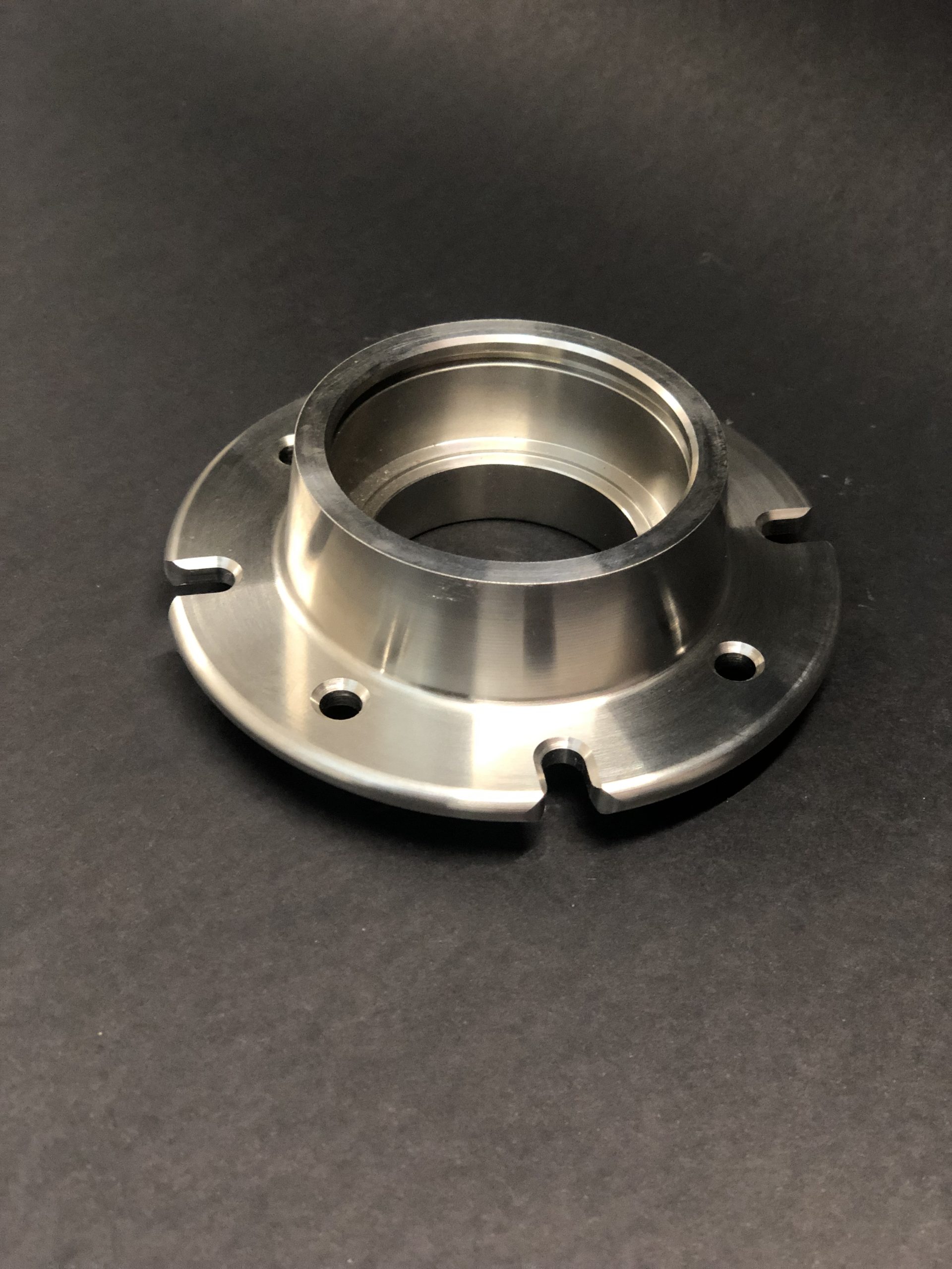 Metal component with a flange, mounting holes and undercuts, made in silver with a glossy finish.