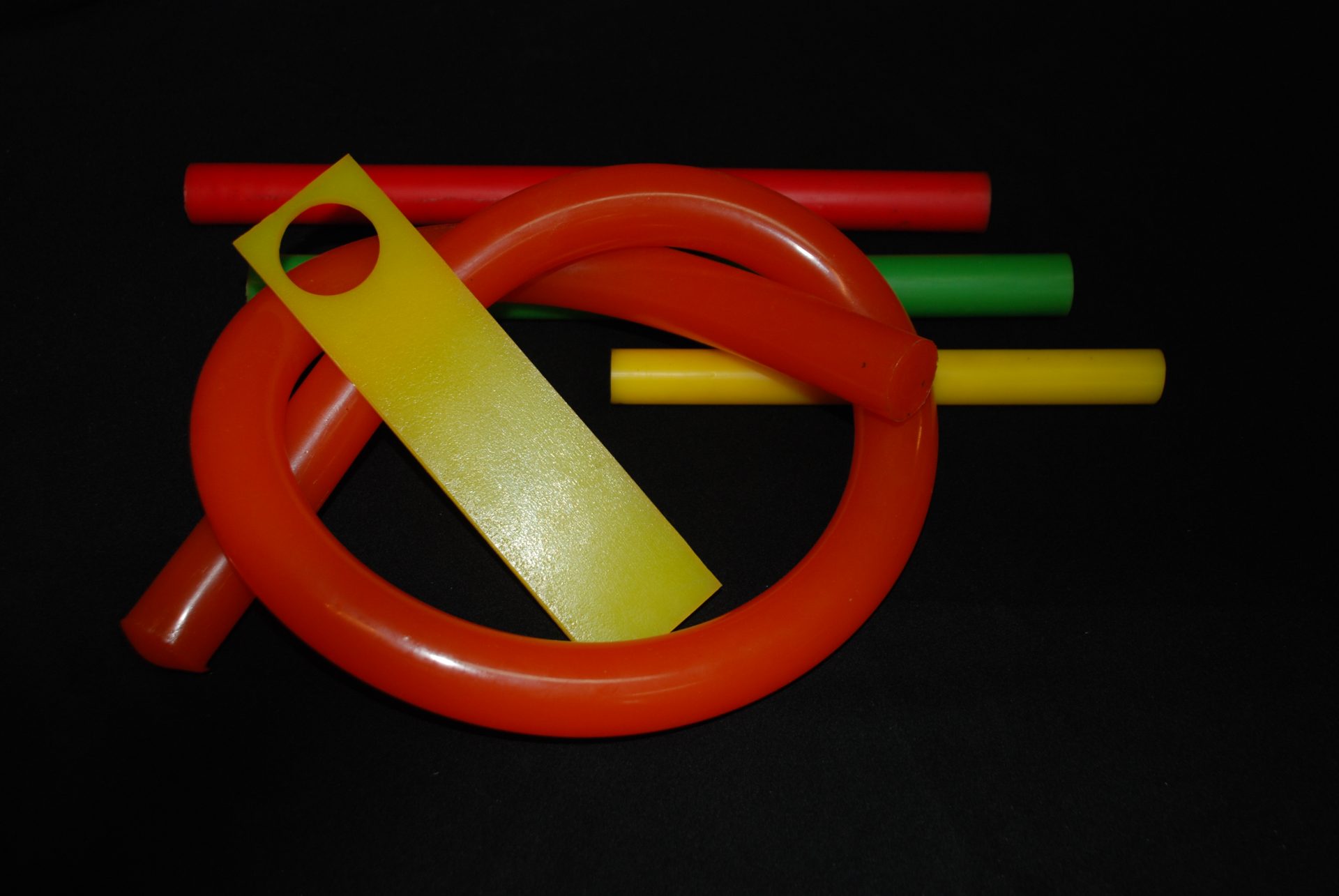 Colourful objects lie on a black background, including red, yellow and green smooth rods and a large red ring.