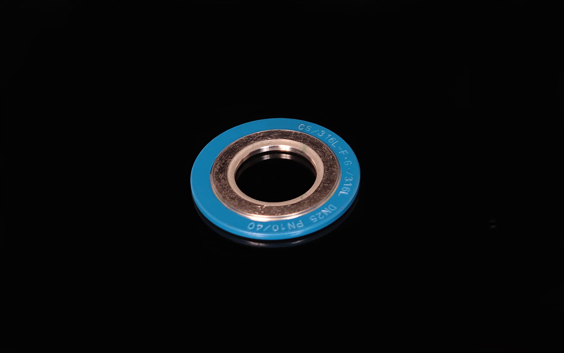 Blue spiral wound gasket with a steel core, lying on a black background with a reflection, with visible lettering and markings.