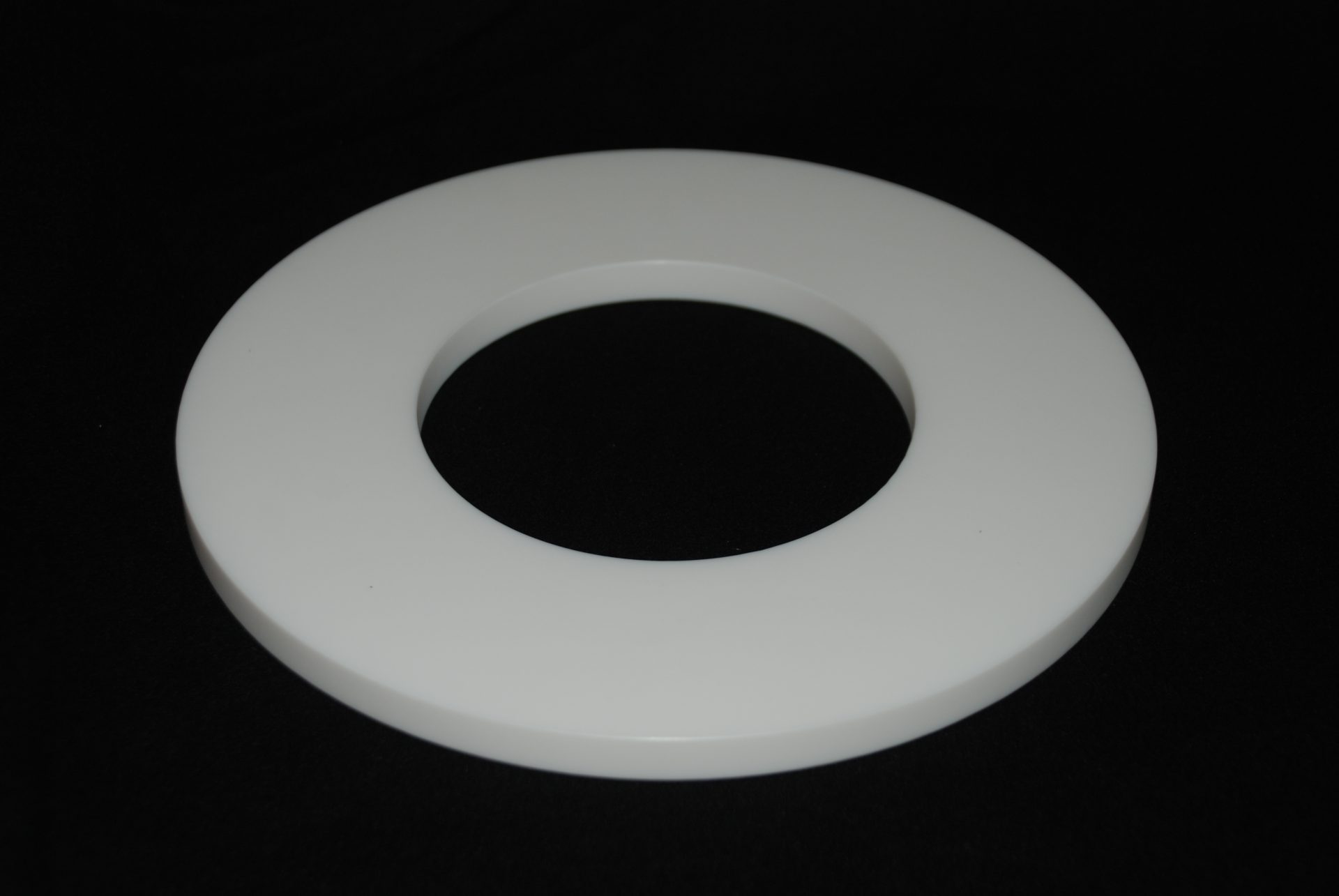 Flat white plastic ring with a large central hole, lying on a deep black background.