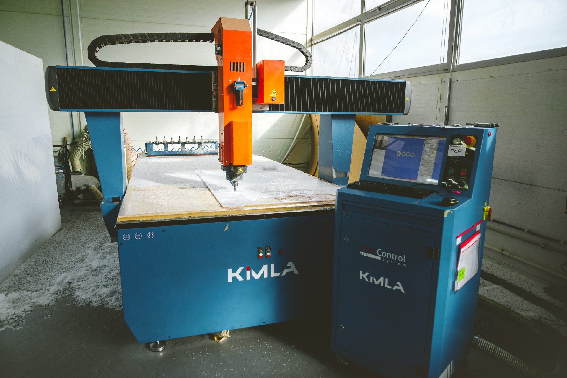 Blue and orange CNC milling plotter with a movable gantry, control panel and work table in the hall.