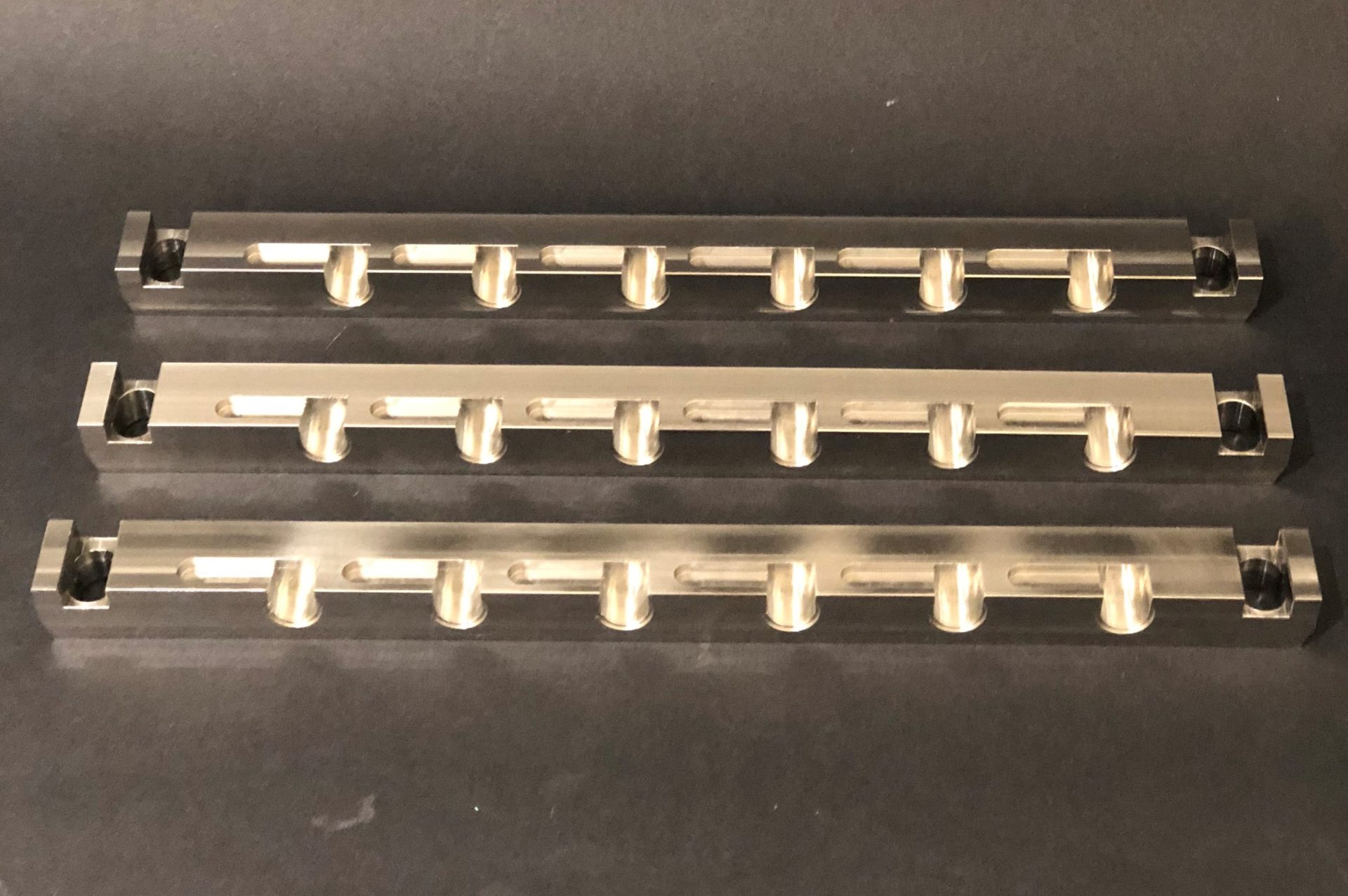 Silvery metal rails with holes and cut-outs lying horizontally on a dark background at even intervals from one another.