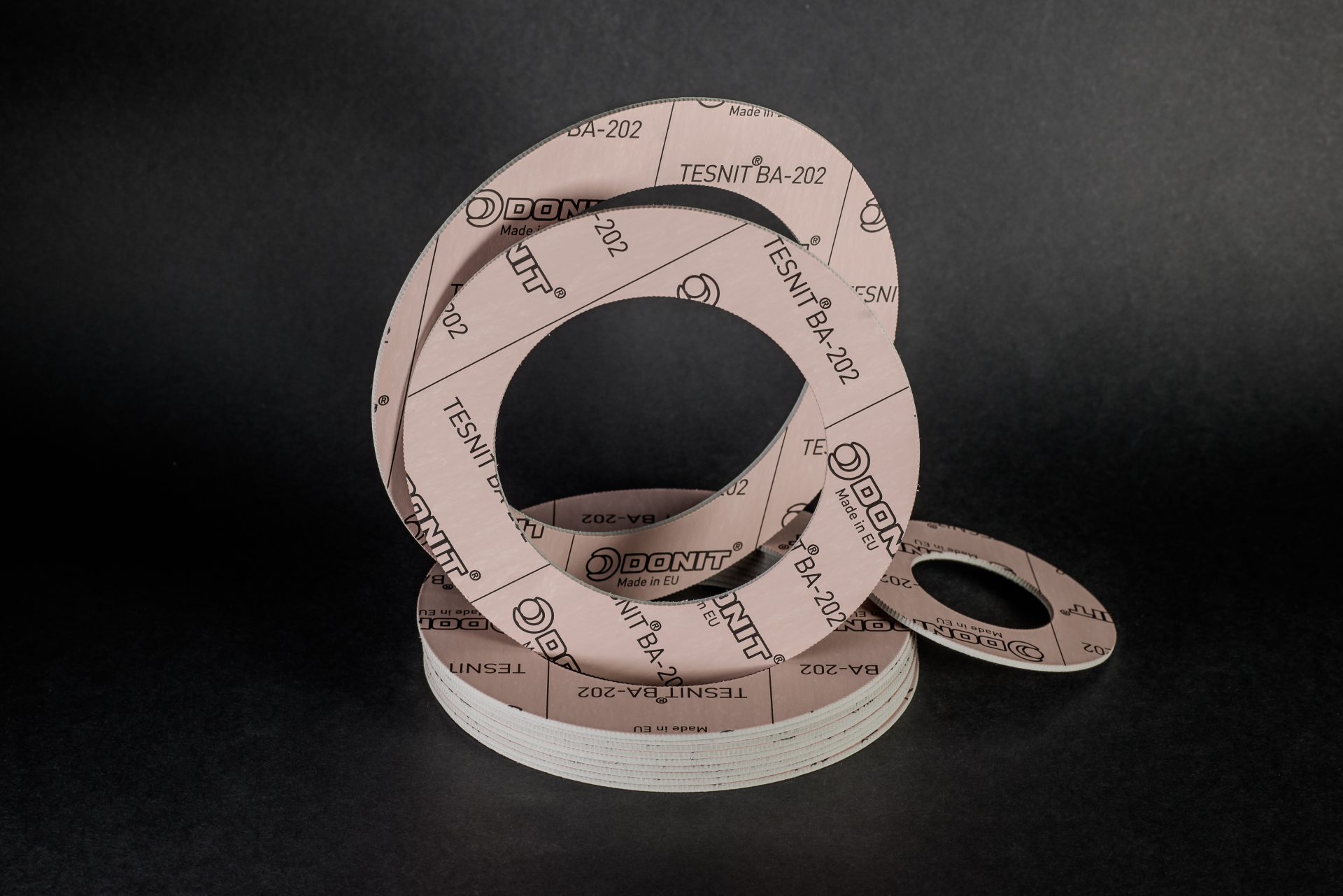 Stack of flange gaskets made of light-coloured gasket sheet with repeated prints, arranged on a black background.