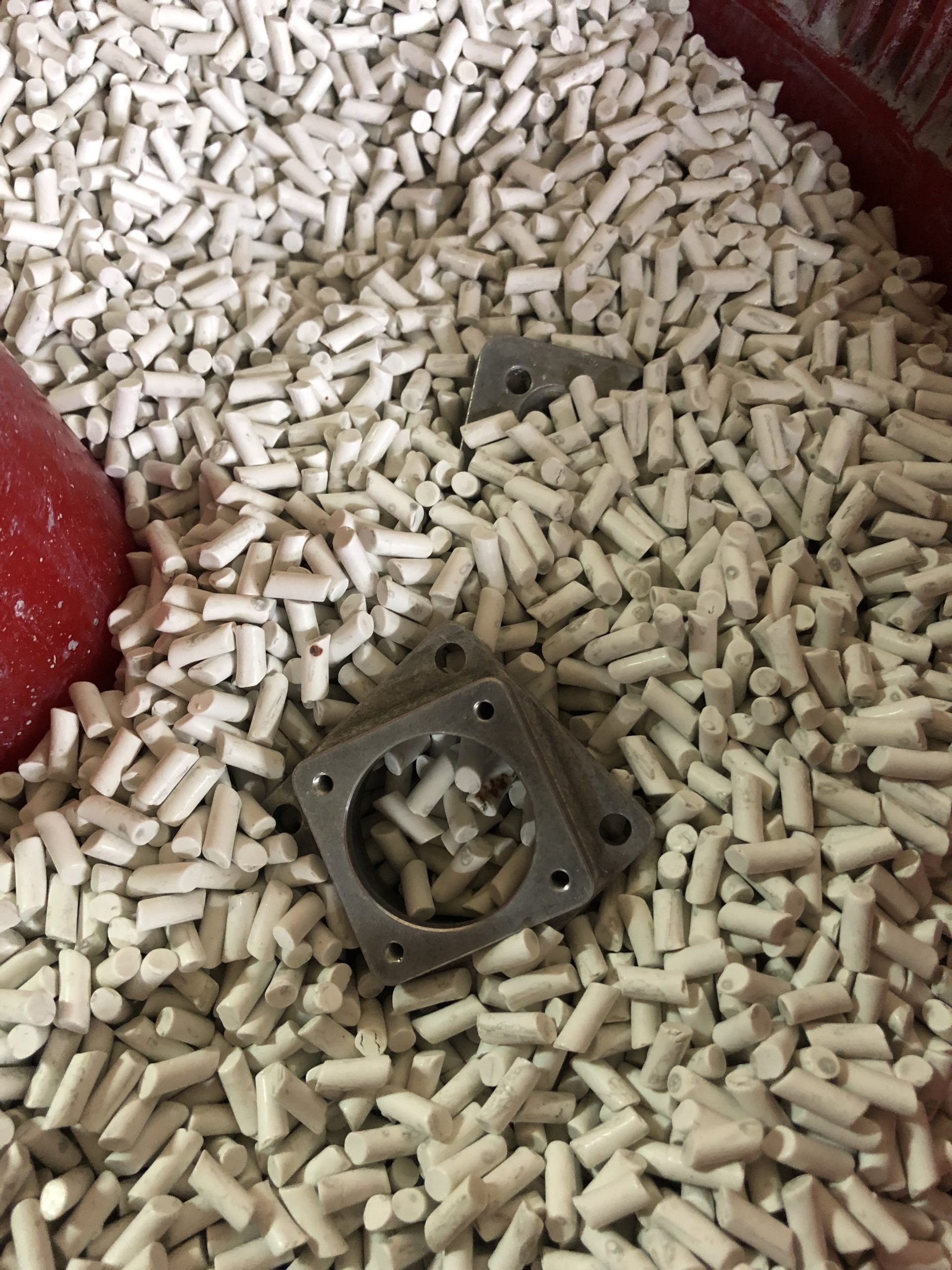 Grey square components with round holes resting on numerous white rollers in a red container.
