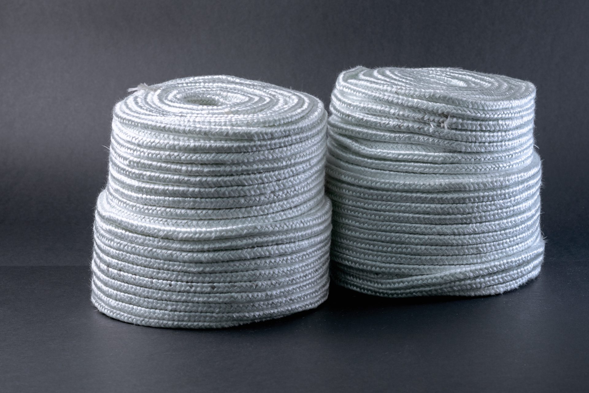 Two coils of white braided fibrous material against a smooth dark-grey background.