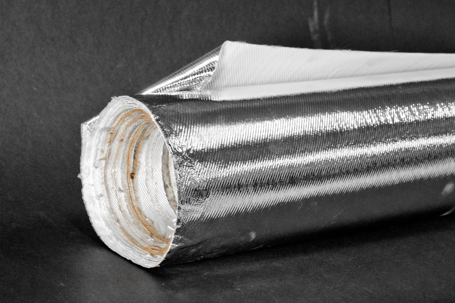 A sheet of material rolled into a coil, with a silver metallic surface and a white textured interior.