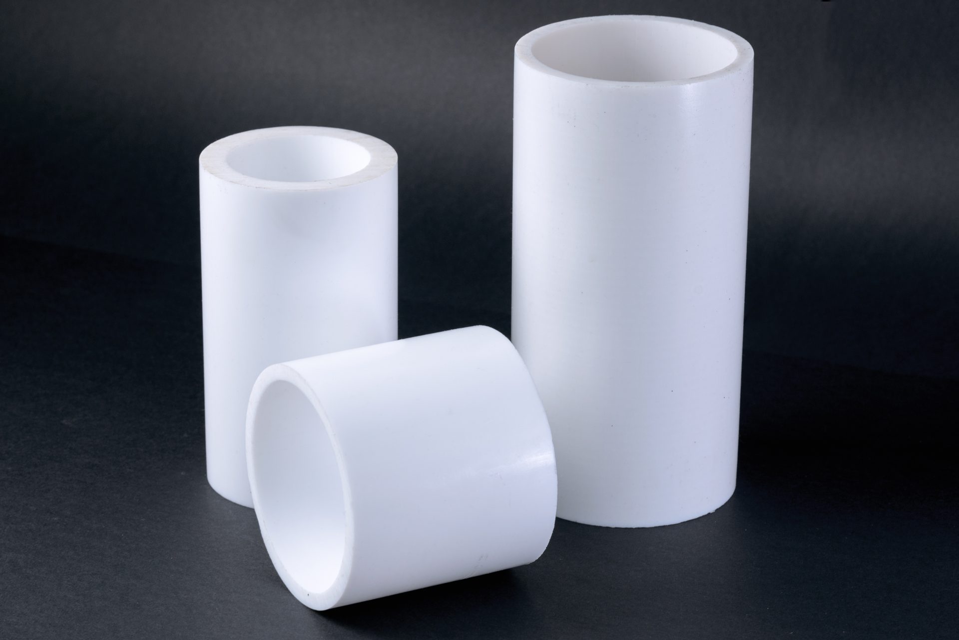 Three white cylindrical plastic bushings of different heights, standing and lying on a dark surface.