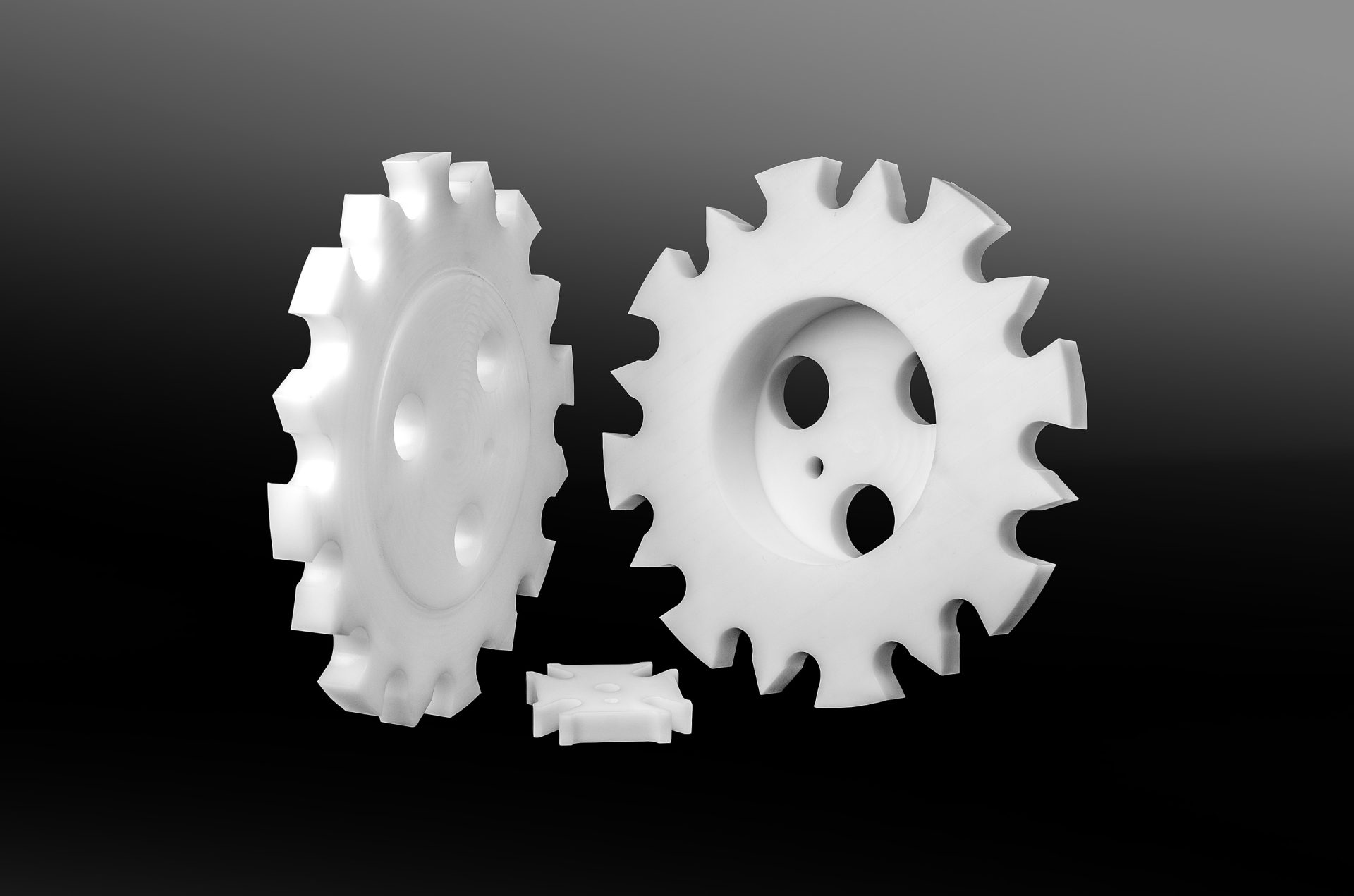 Three white plastic sprockets with holes and evenly spaced teeth on a dark background.