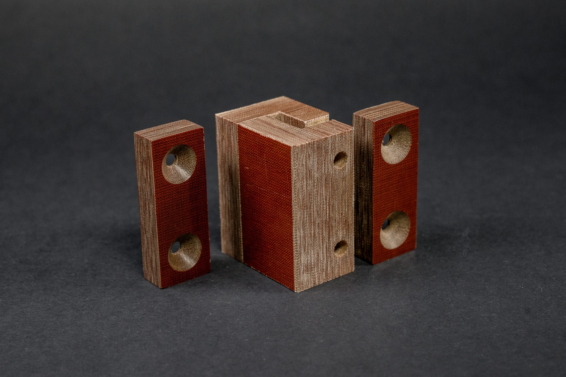 Three brown blocks stand against a grey background; the left and right ones have chamfered holes, and the middle one is slid apart from them.