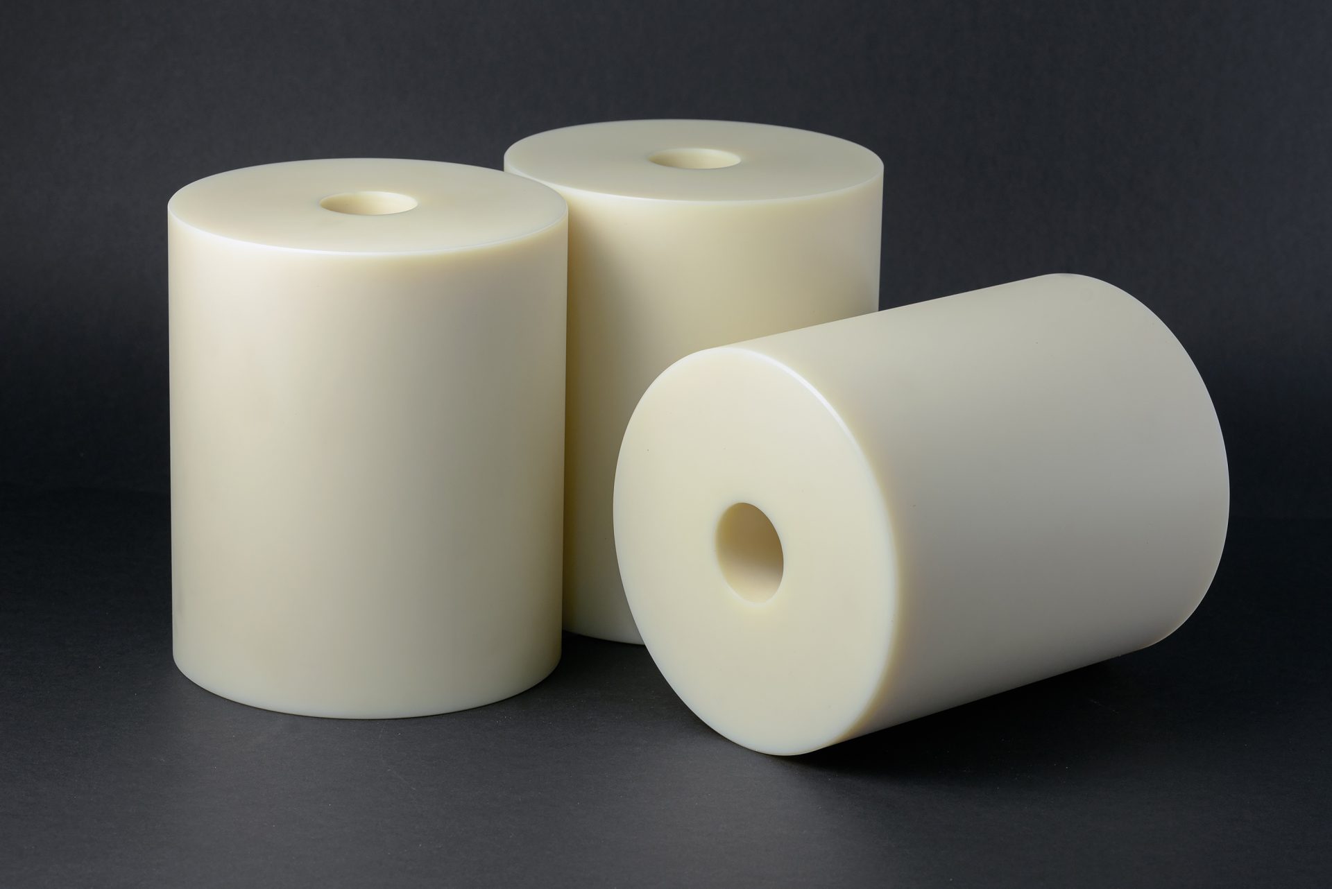 Three cream-coloured plastic cylinders with smooth surfaces and central bores standing against a dark background.
