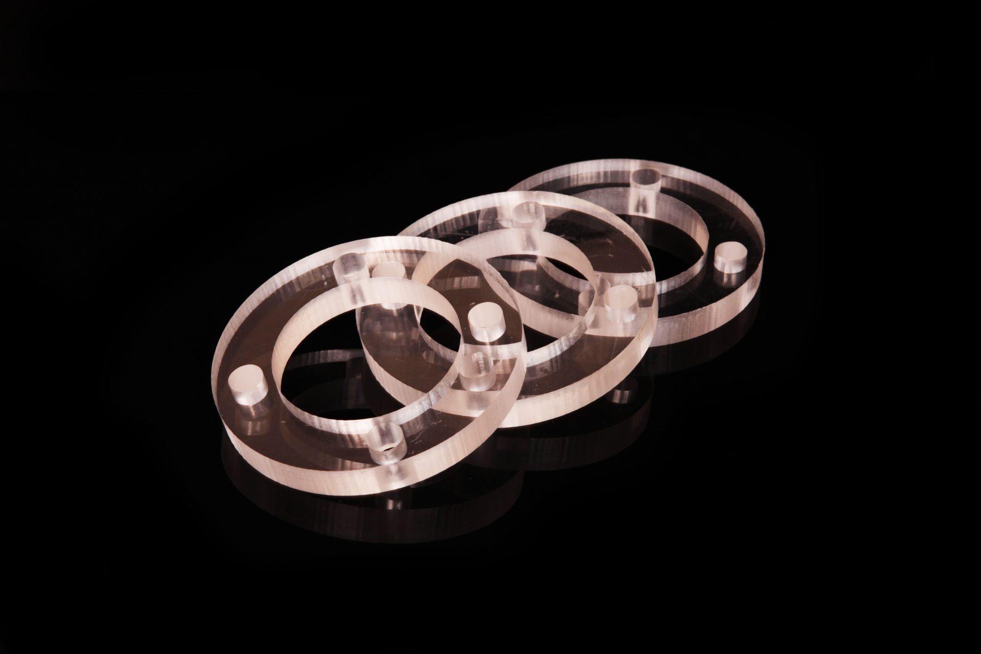 Three transparent ring-shaped parts with small lugs arranged on a black surface with a reflection.