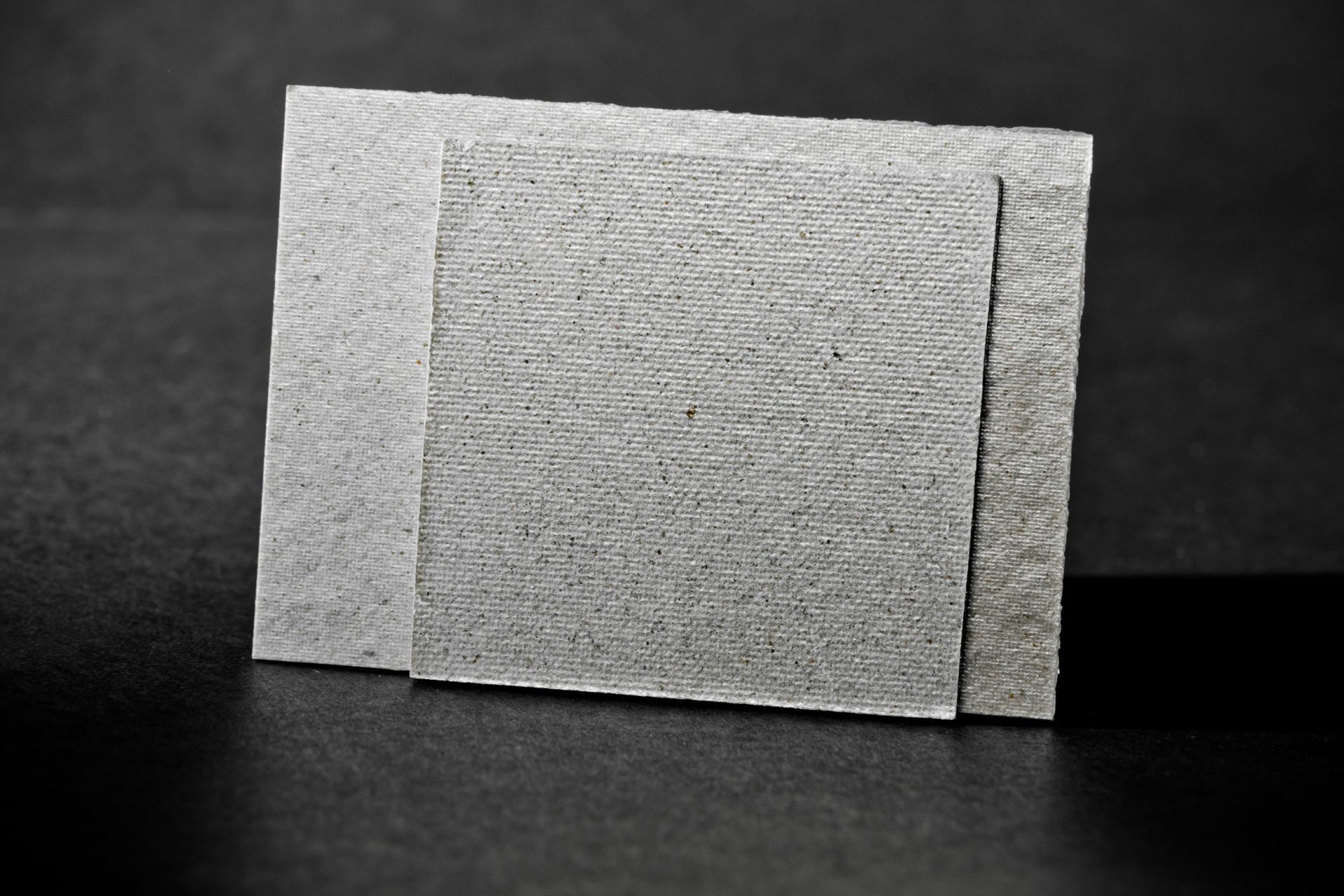 Three rectangular grey insulation boards with varied fine-grained surfaces standing against a dark background.