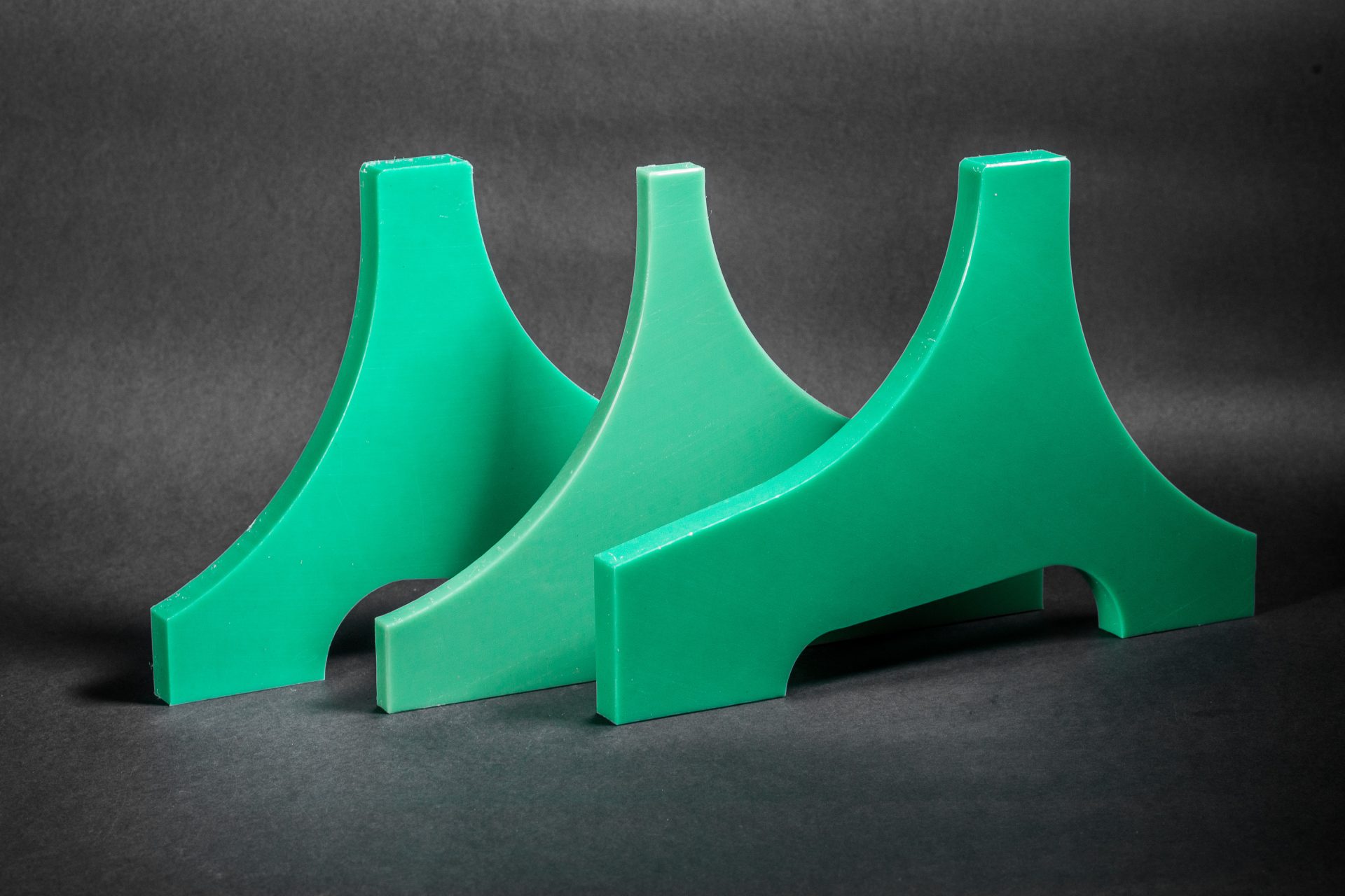 Three green profiled plastic brackets with arched cut-outs standing against a dark background.
